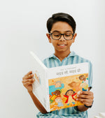 Load image into Gallery viewer, Child holding the bilingual Hindi English children’s book Pay It Forward, showing both the front and back covers with colorful illustrations and Hindi–English text.
