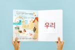 Load image into Gallery viewer, Inside lift‑the‑flap page from the bilingual Korean–English children’s book Pay It Forward showing a city scene and a vocabulary word with Korean Hangul and English text for early readers.
